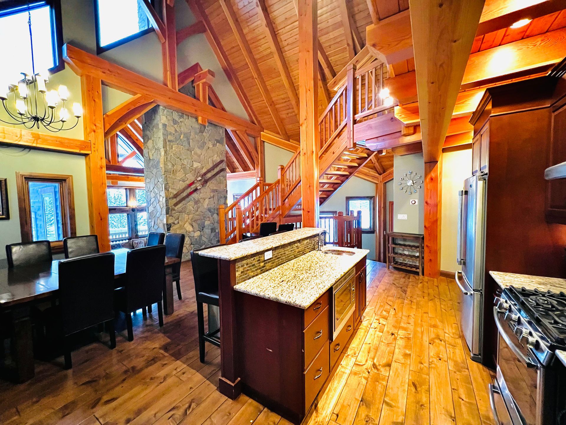 Rustic lodge interior with wood beams, stone fireplace, kitchen island, and dining area with high ceilings
