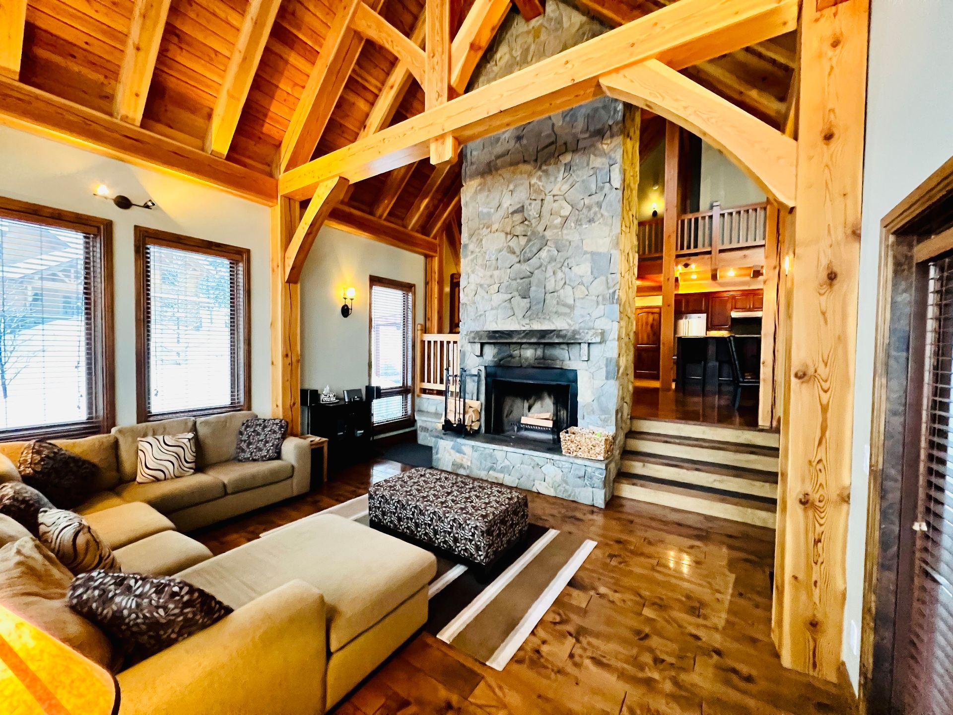 Cozy living room with exposed wood beams, stone fireplace, and large windows overlooking snowy scenery
