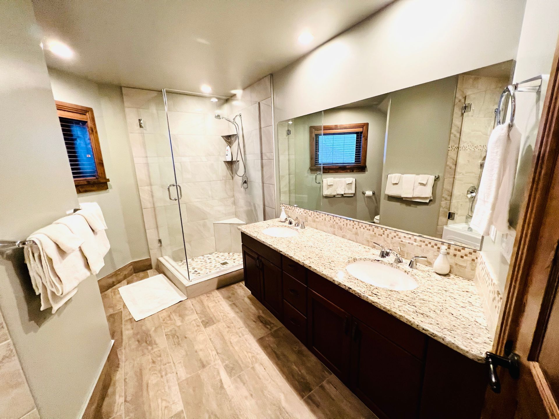 Modern bathroom with double vanity, large mirror, glass shower, and wood-look tile floor