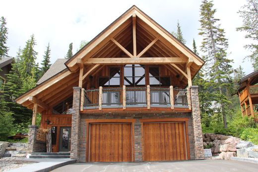Rustic wooden mountain cabin with stone accents, large balcony, and double garage, surrounded by pines