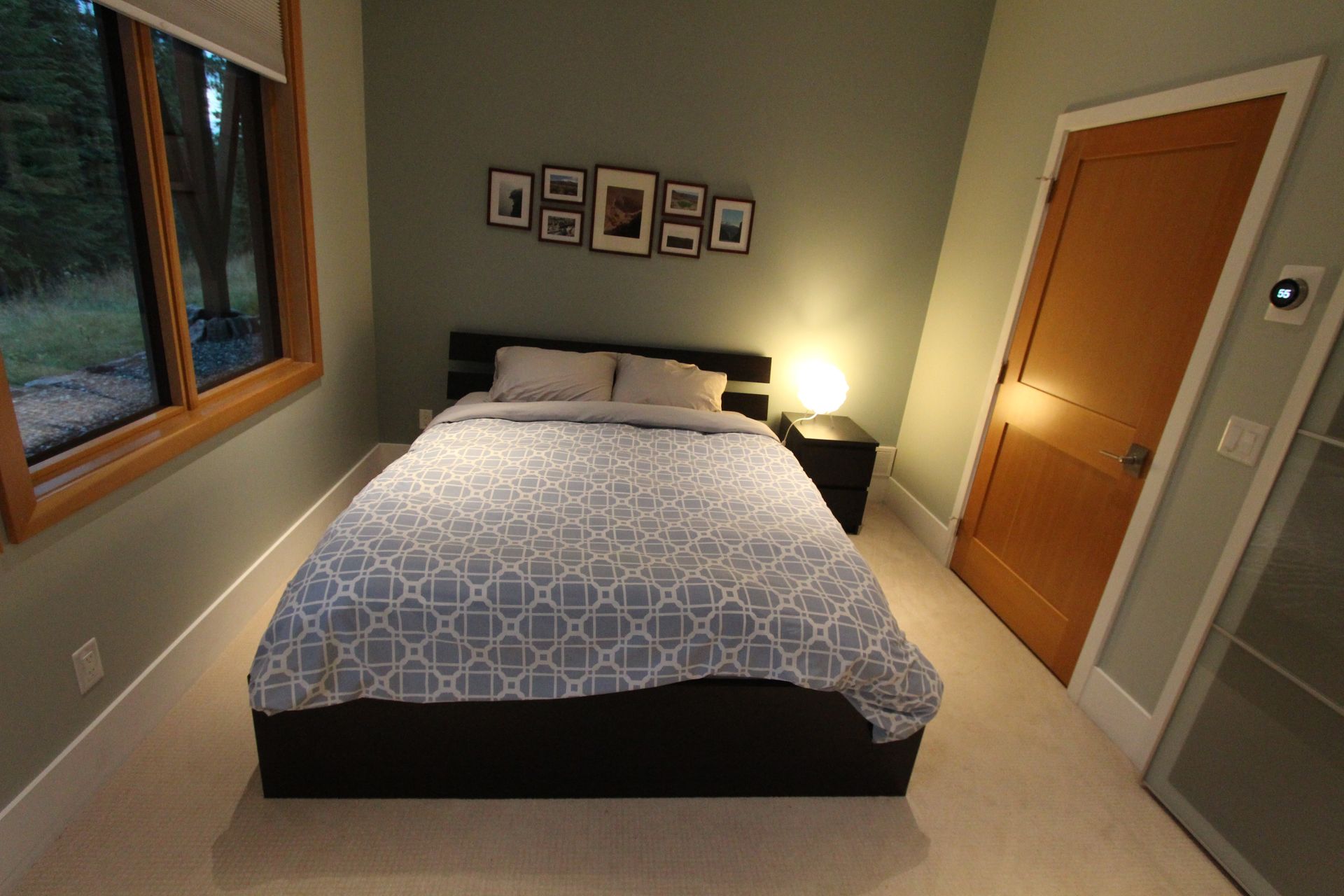 Cozy bedroom with a made bed, bedside lamp, wall art, and window overlooking greenery