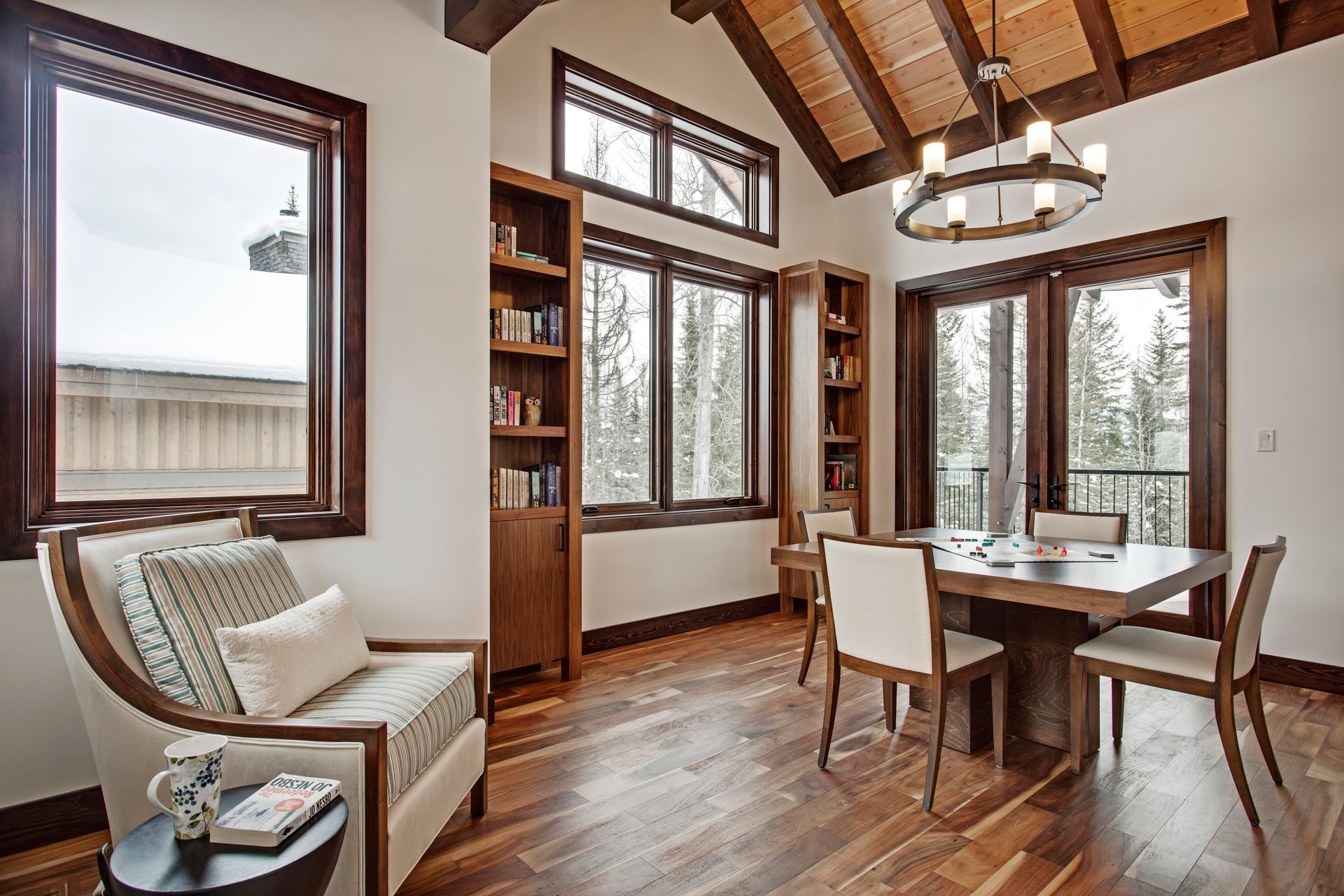 Bright dining room with wood beams, large windows, a table, chairs, and a cozy armchair.