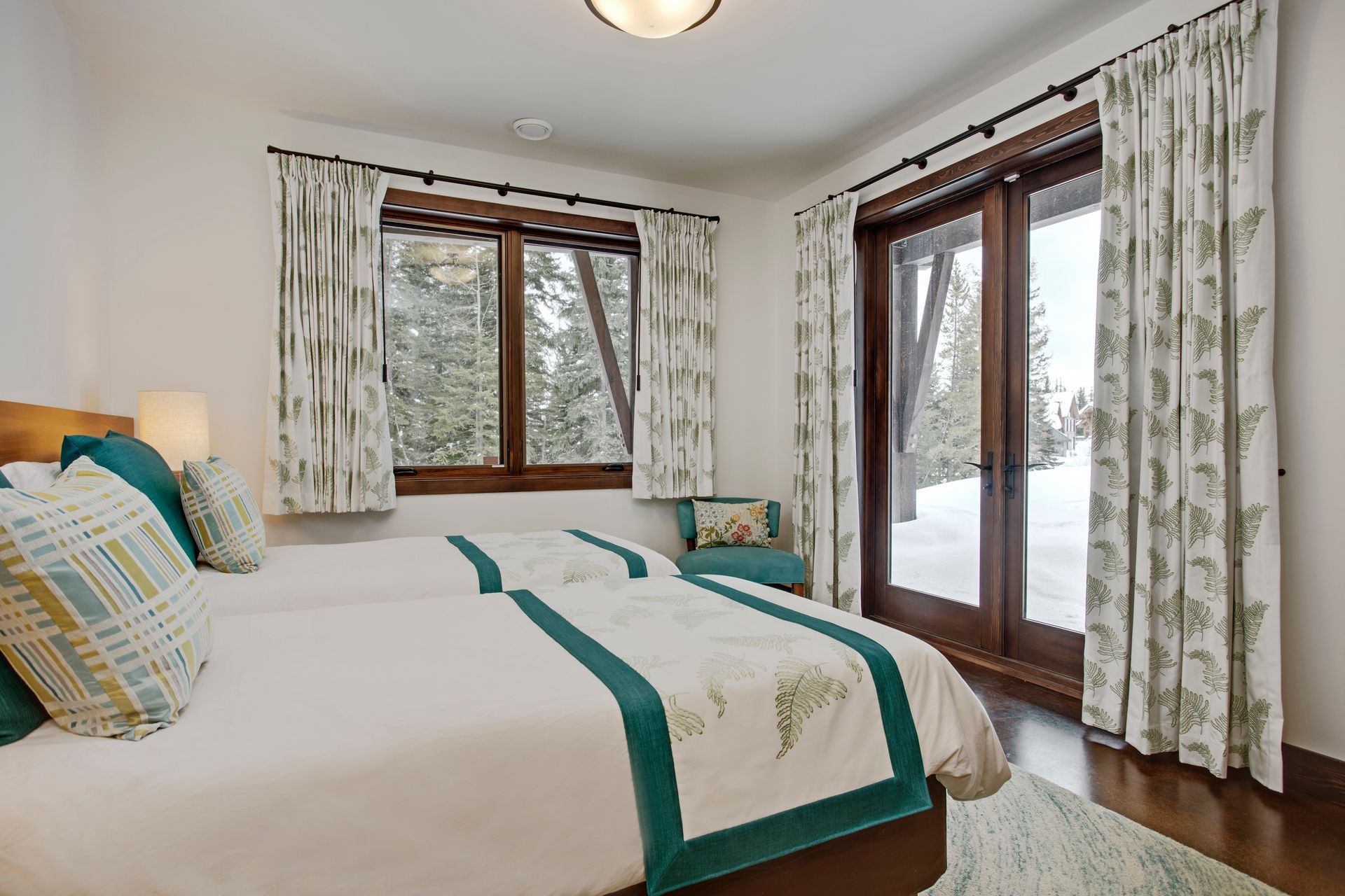 Bright bedroom with a made bed, teal accents, and large windows with curtains