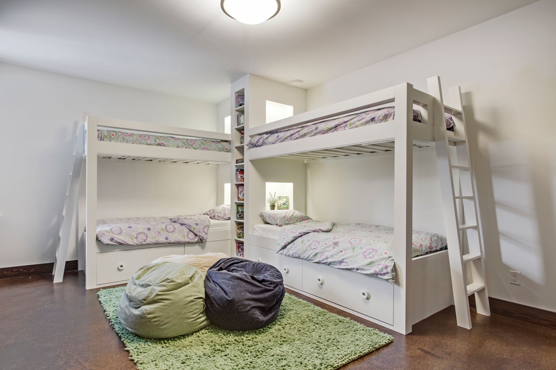 Bright kids' bedroom with two white bunk beds, green rug, and bean bags on the floor