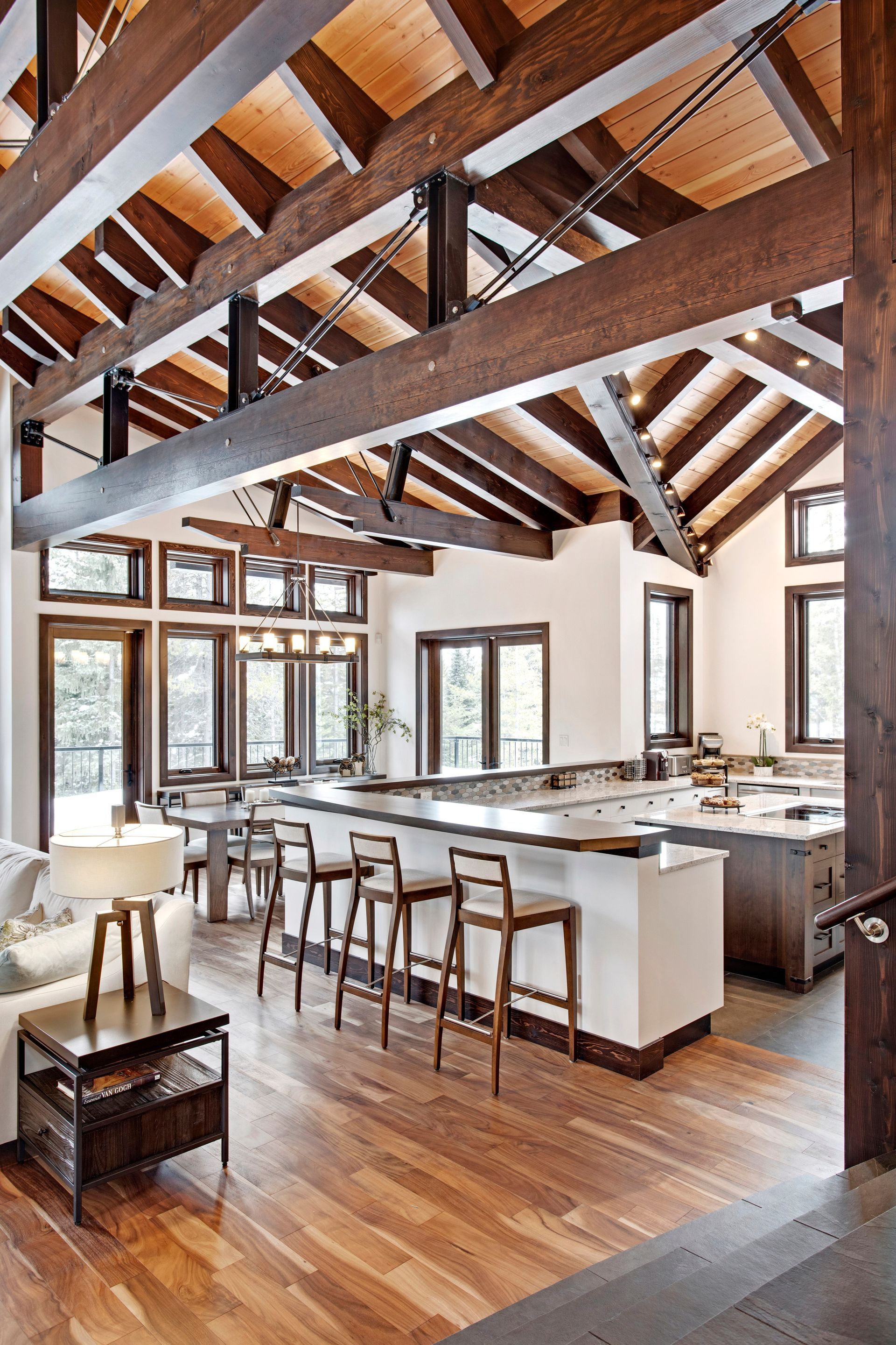 Bright open kitchen with exposed wooden beams, island seating, and large windows over hardwood floors