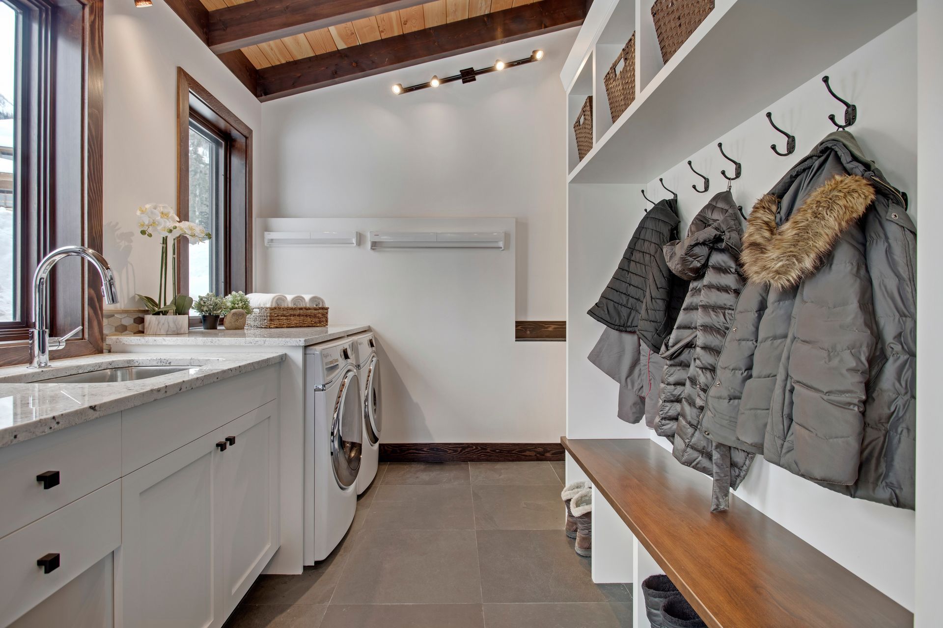 Bright mudroom-laundry with white cabinets, washer, built-in cubbies, and hanging coats and hats