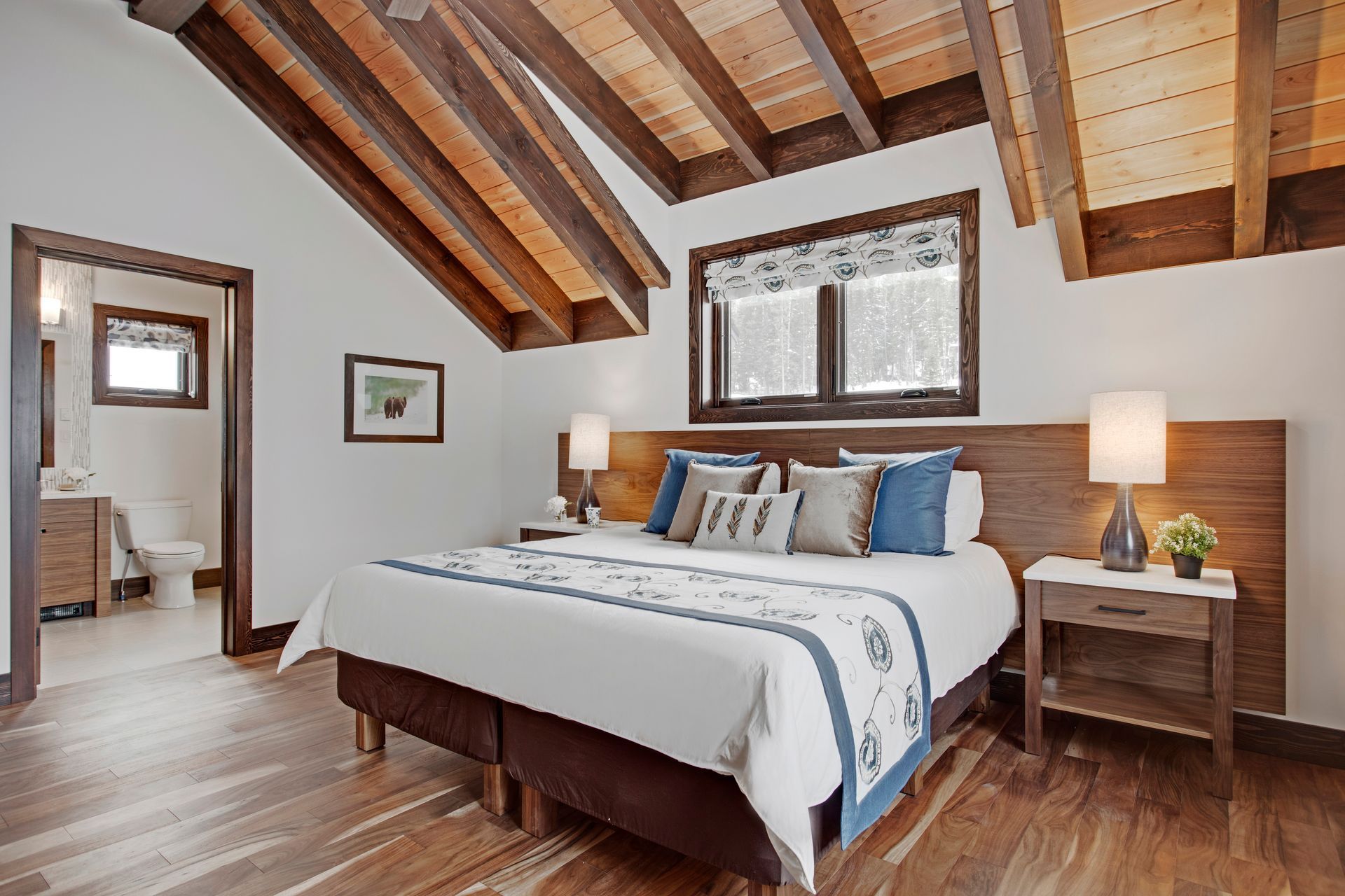 Cozy bedroom with sloped wood ceiling, queen bed, nightstands, and soft natural light