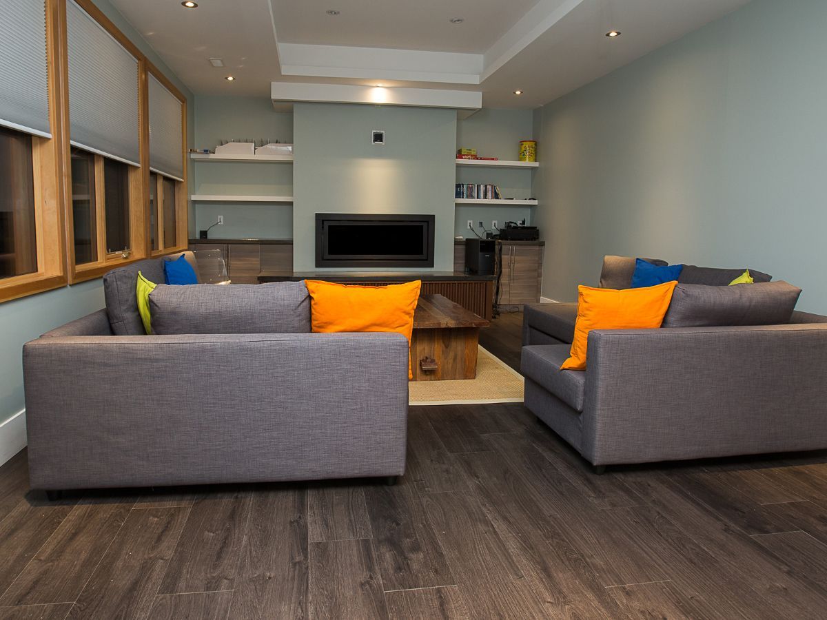 Modern living room with gray sofas, orange cushions, fireplace, and dark wood floor.