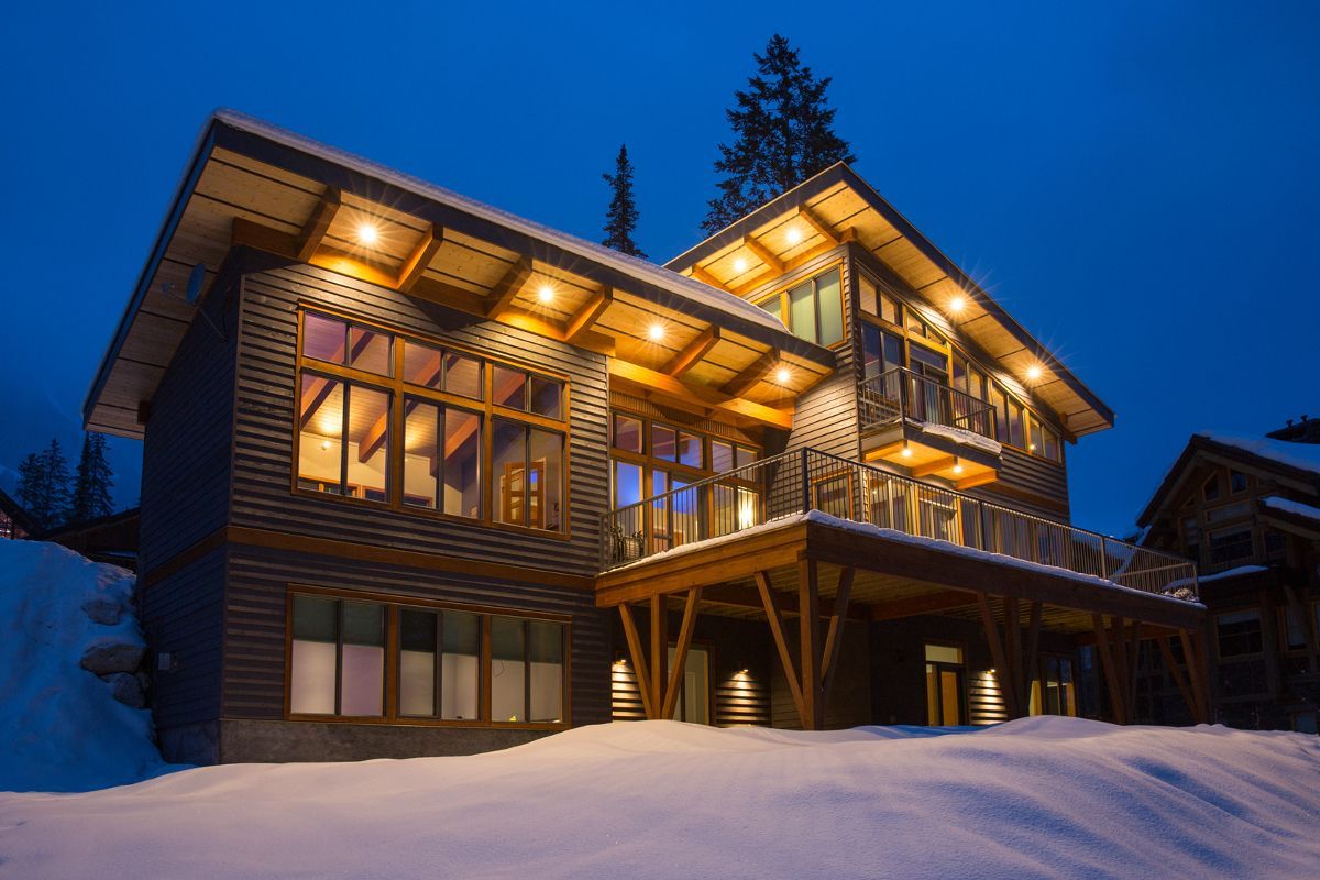 Snowy mountain lodge glowing warmly at dusk, with large windows and wooden balconies.