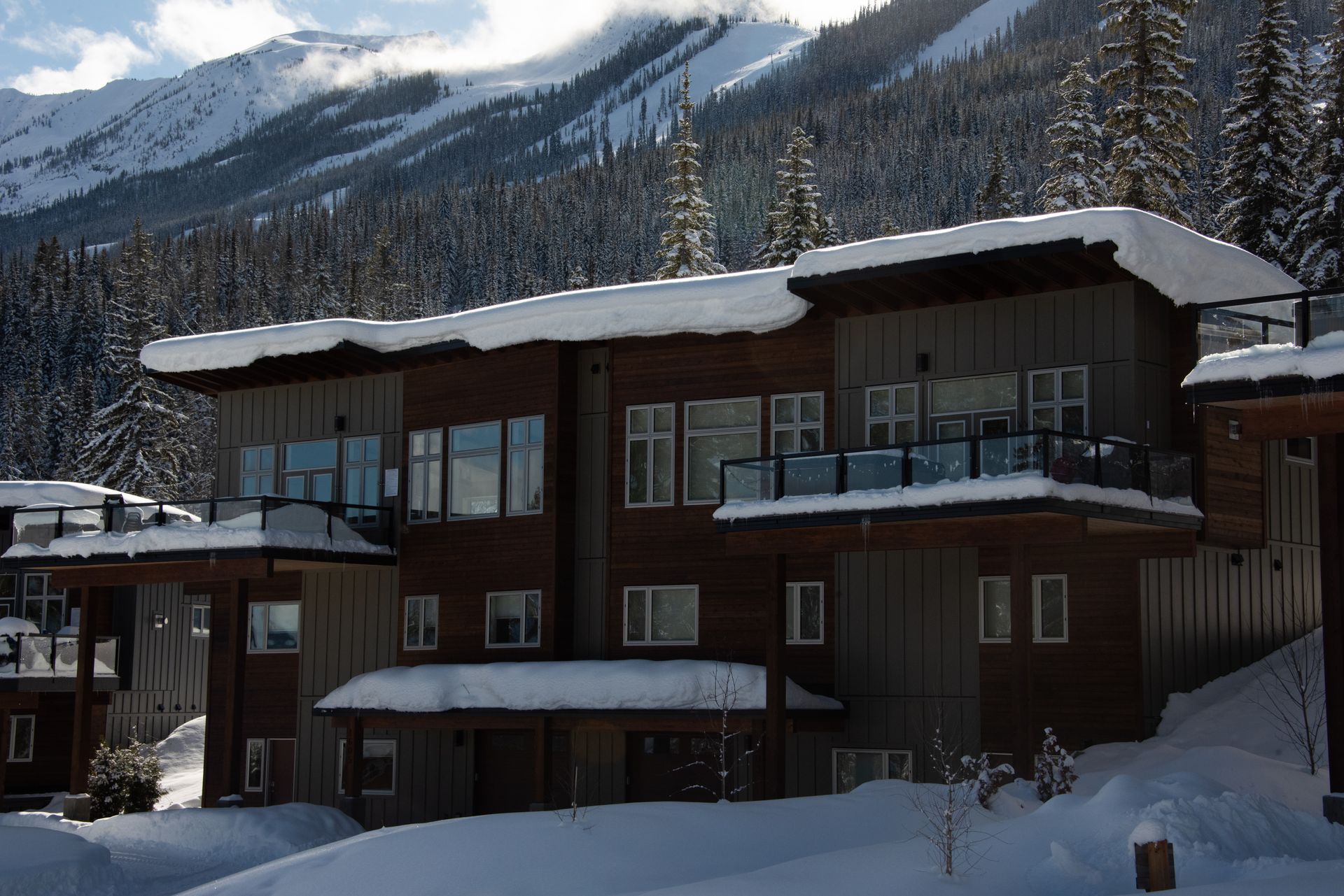 Snow-covered chalet-style building with balconies and mountains in the background