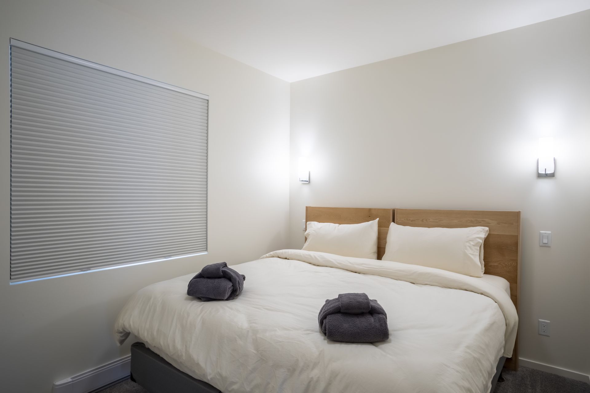 Neat bedroom with a bed, white bedding, two gray towels, and a window with blinds.
