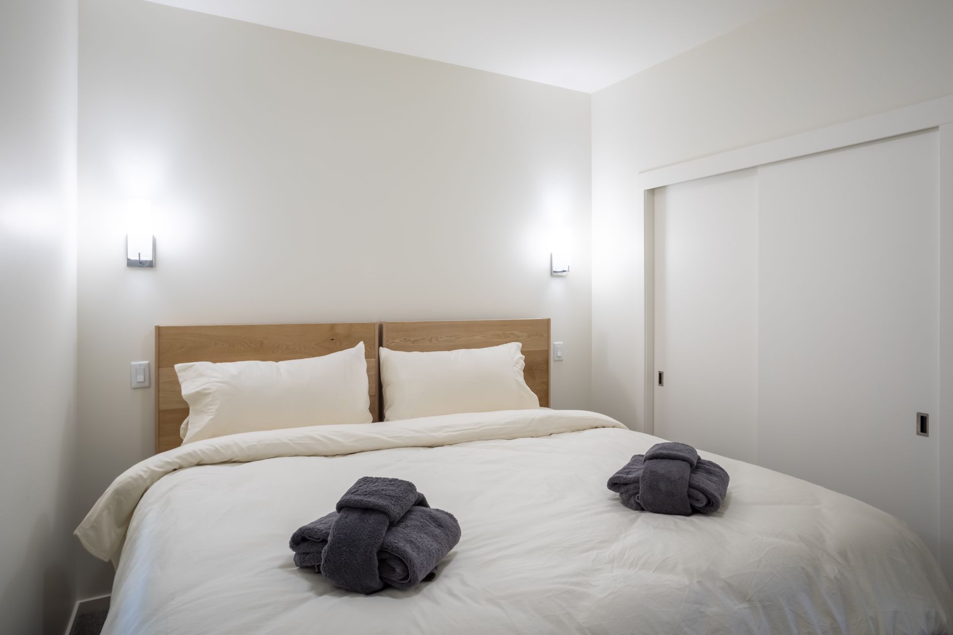 Neatly made bed with folded towels in a minimalist white bedroom