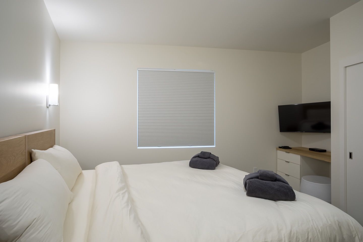 Minimal white bedroom with bed, blinds, and wall-mounted TV