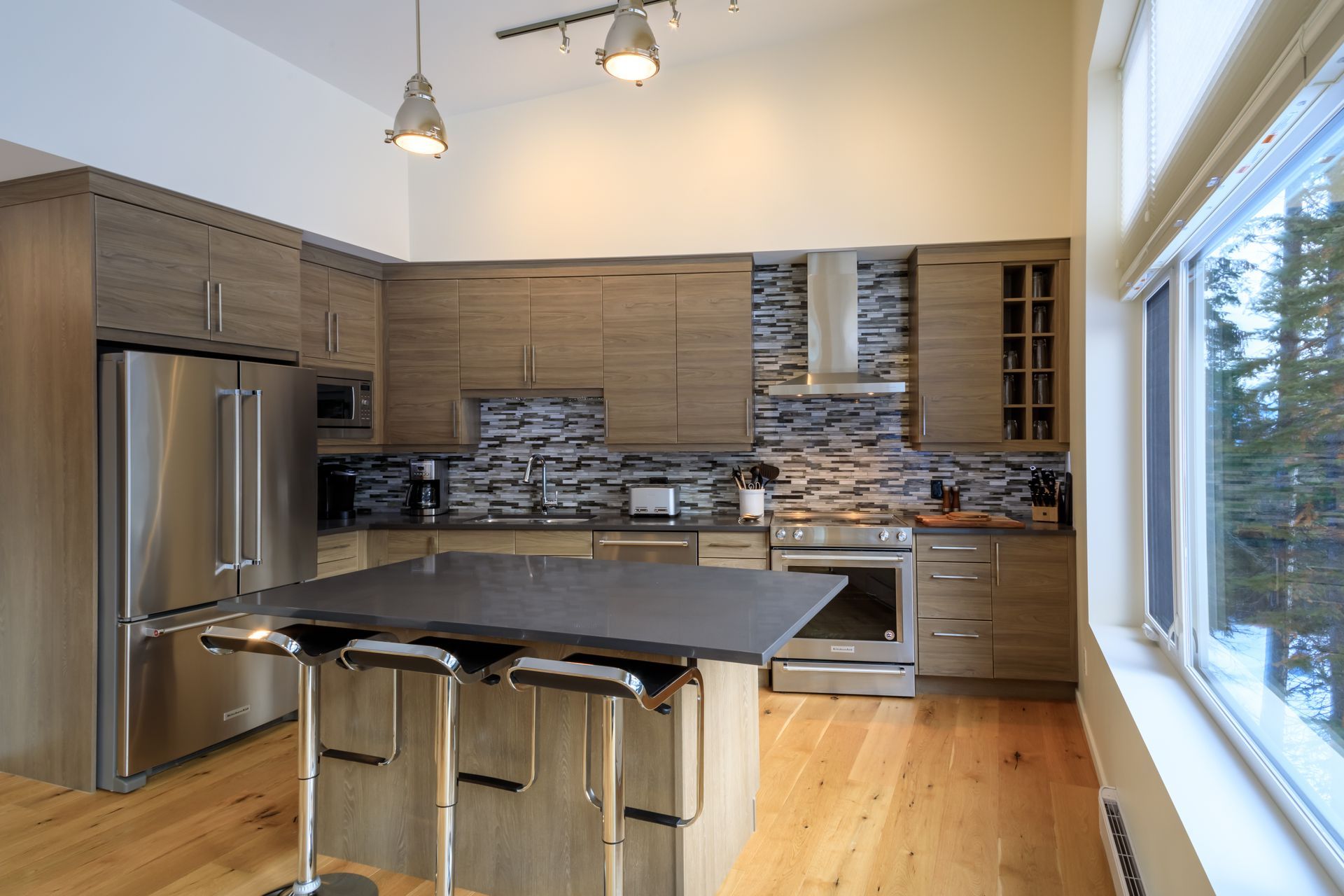 Modern kitchen with stainless appliances, wood cabinets, island, stone backsplash, and large window