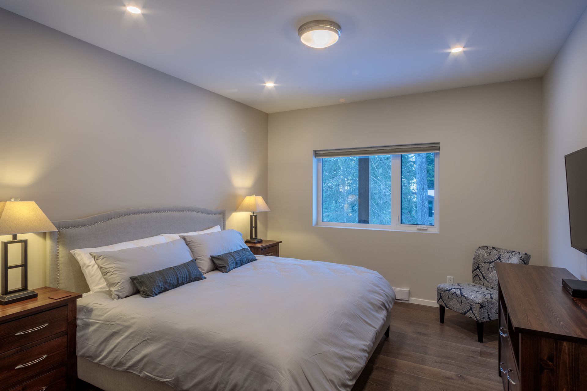 Bright bedroom with a large bed, bedside lamps, window, and wooden dresser in neutral tones