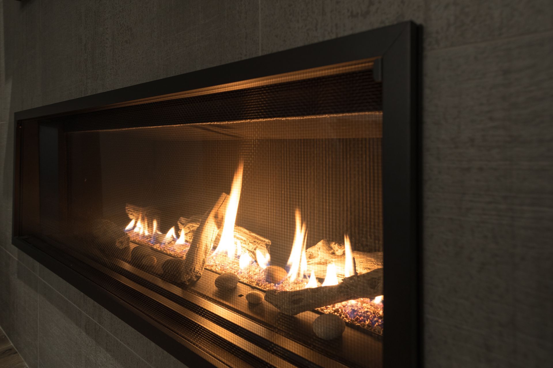 Modern linear gas fireplace with flames behind a glass screen in a dark wall niche