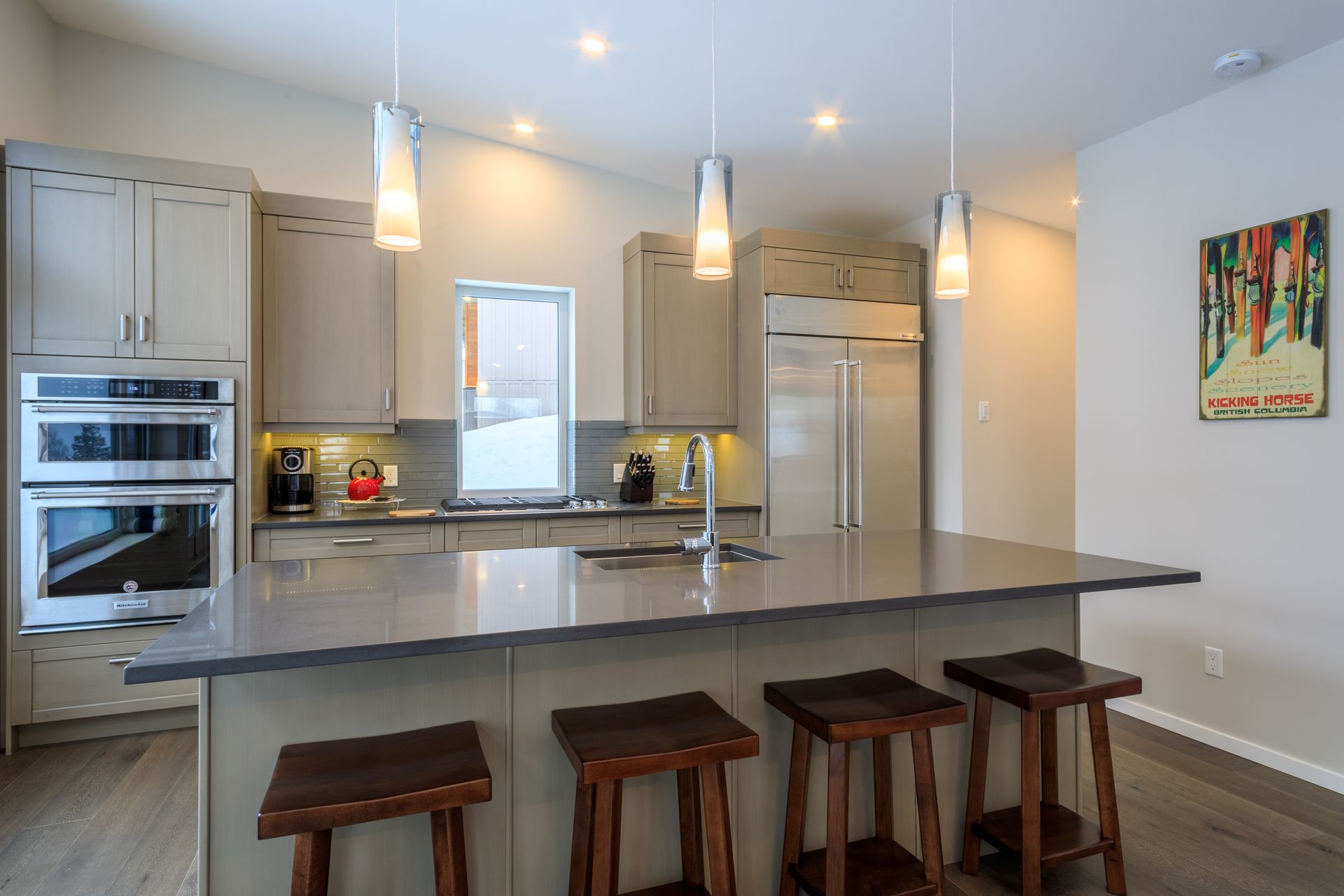 Modern kitchen with large island, pendant lights, stainless appliances, and four wooden stools