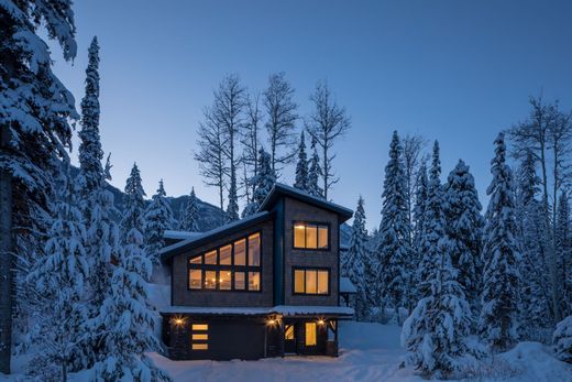 Cozy lit cabin in snowy forest at dusk with tall pine trees surrounding it