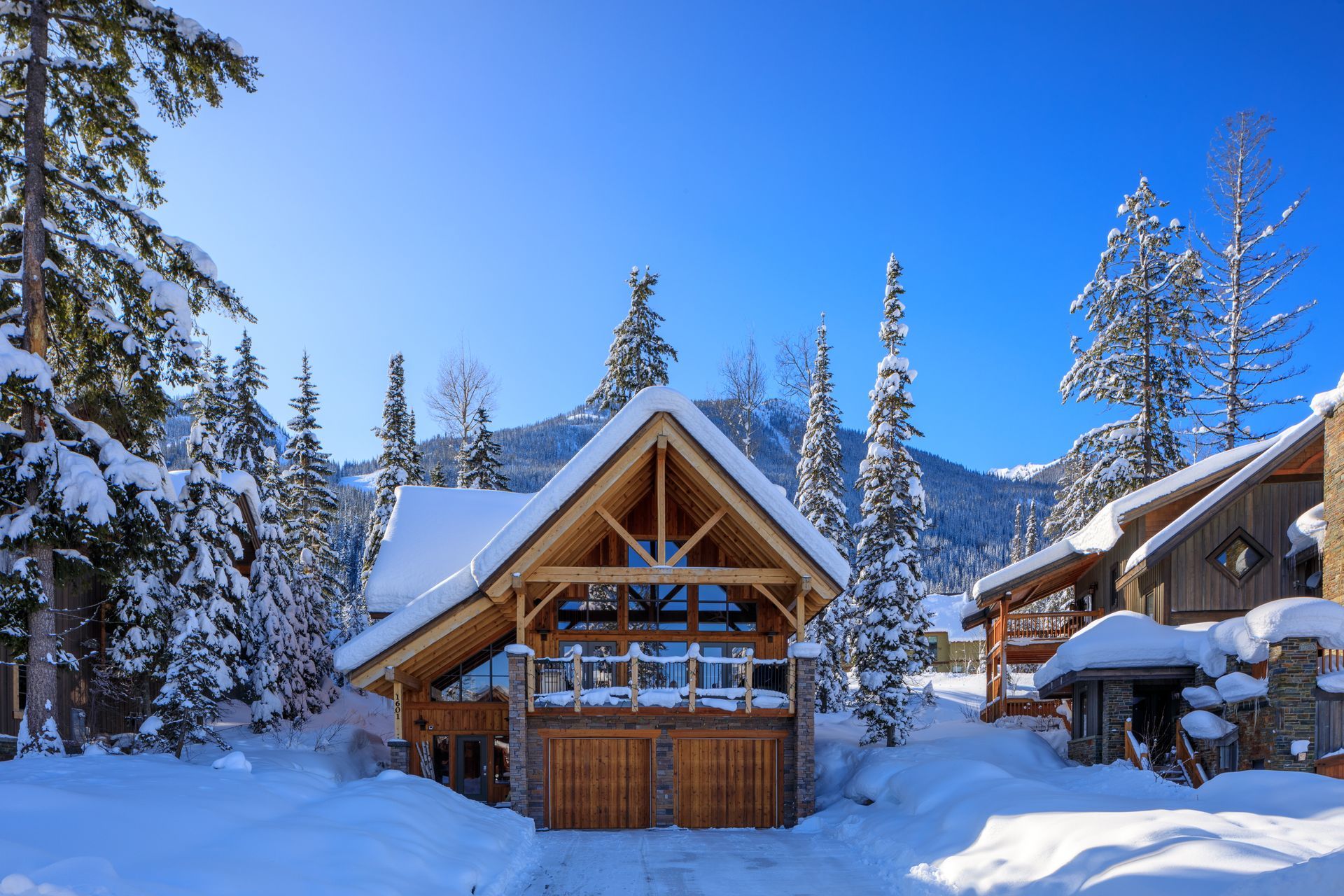 Snowy mountain cabins under a clear blue sky, surrounded by pine trees.