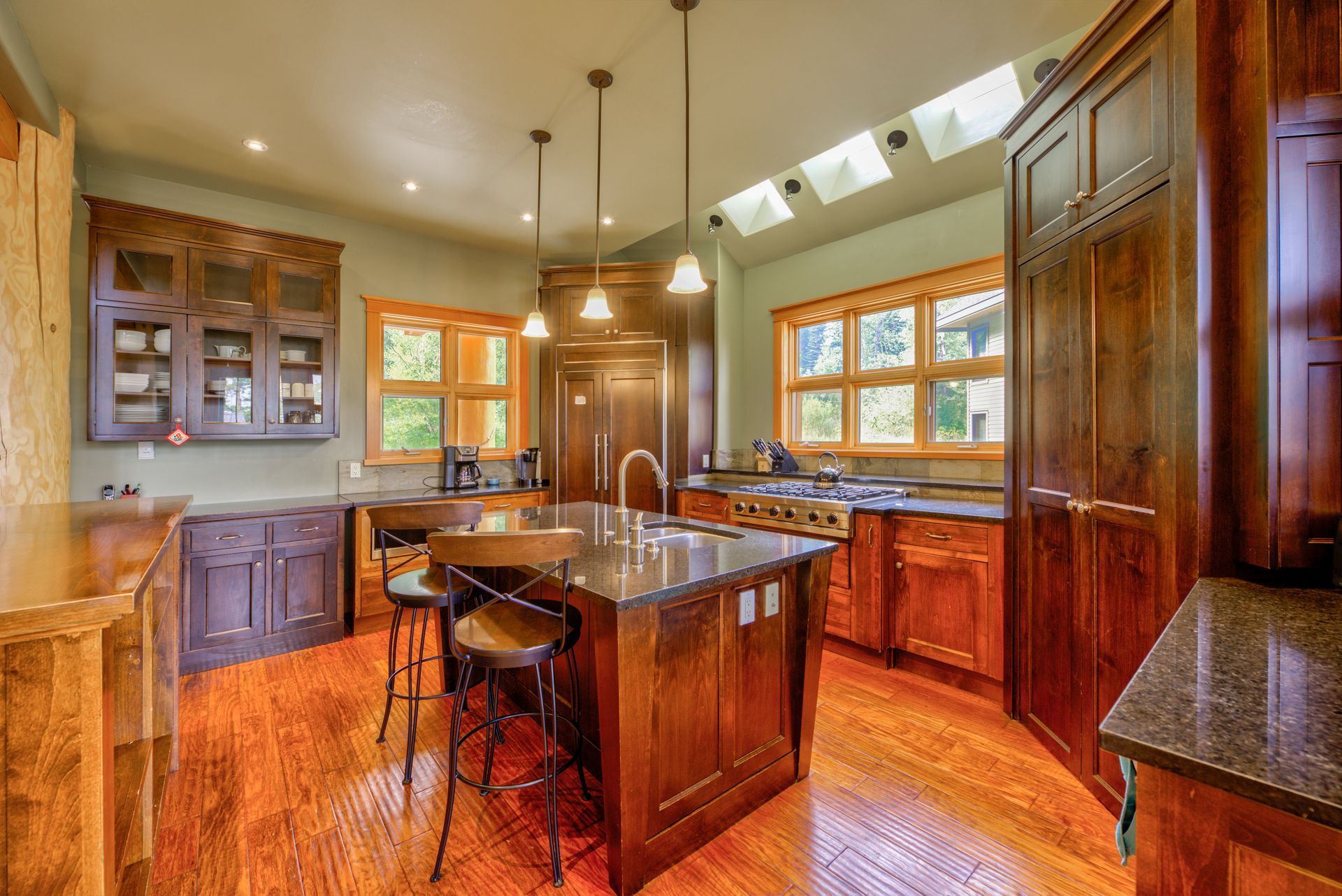 Warm wooden kitchen with central island, cabinets, and large windows letting in natural light
