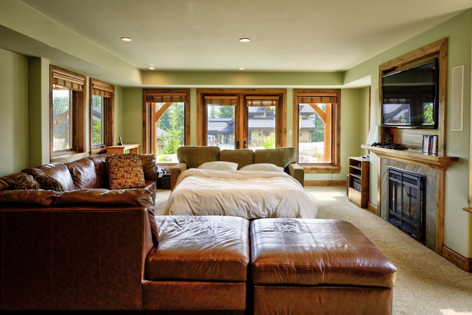 Spacious bedroom with large windows, a bed, leather seating, and a fireplace-mounted TV.