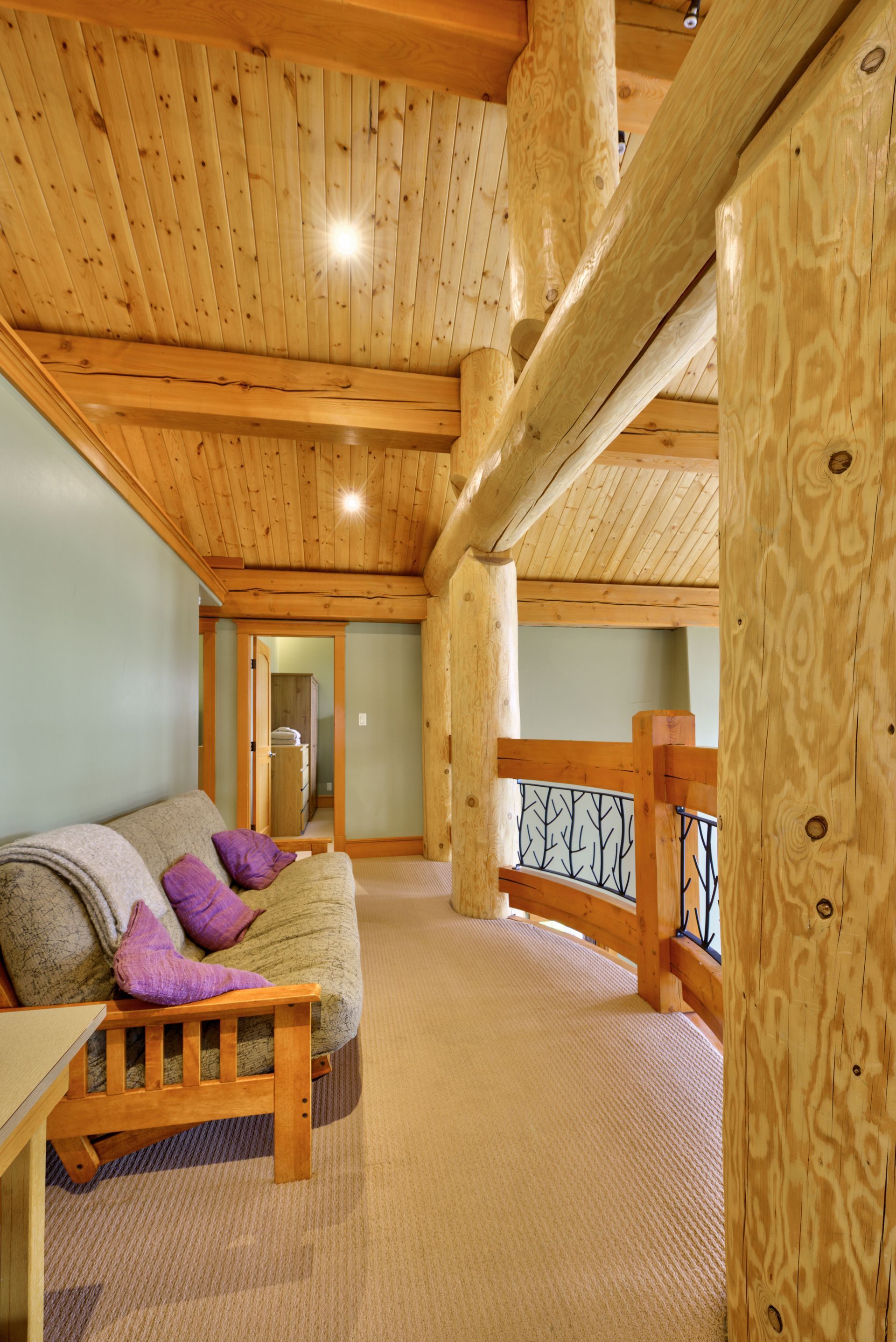 Loft living room with wood beams, beige sofa, and railing overlooking the lower floor