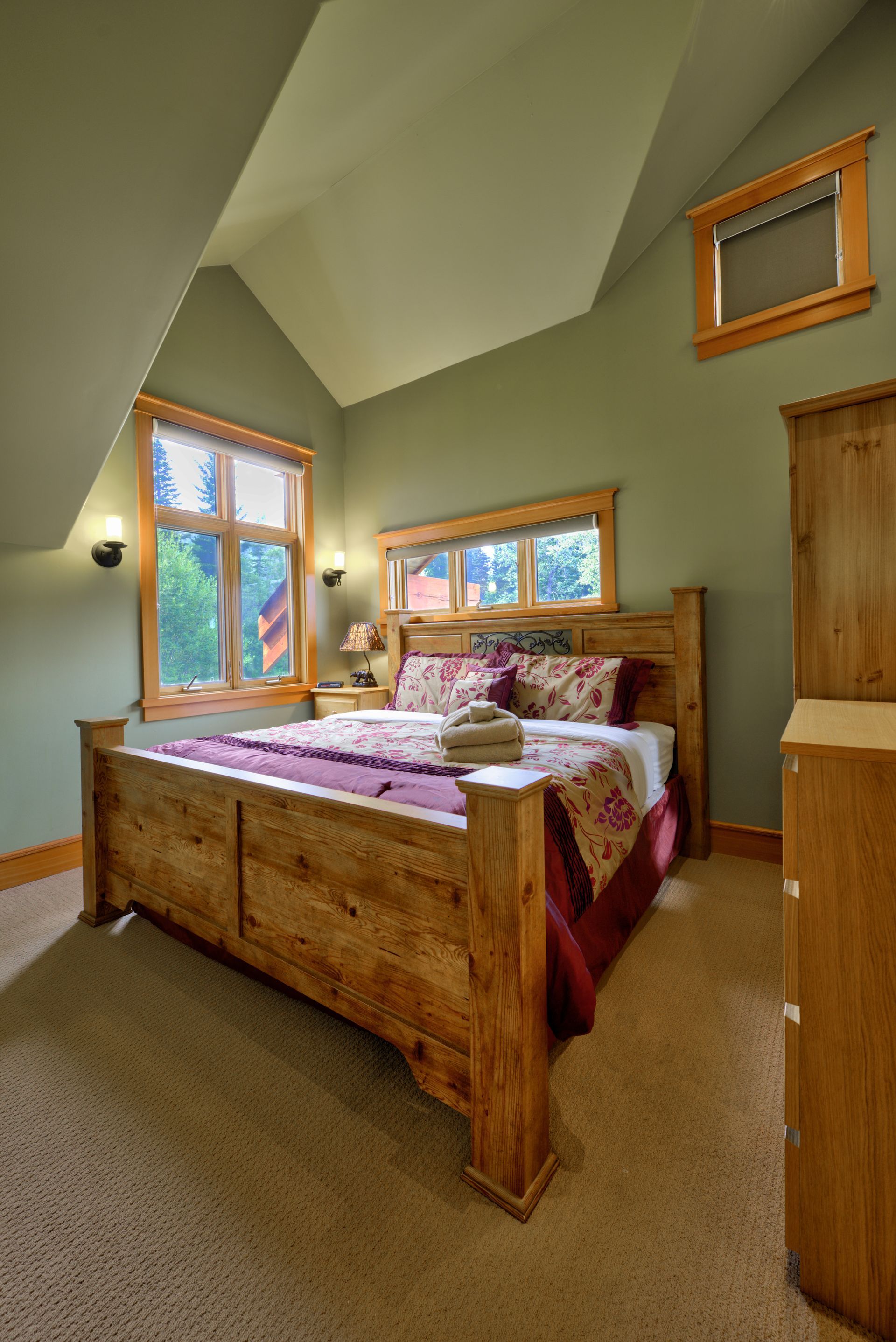 Cozy attic bedroom with a wooden bed, colorful quilt, and slanted ceiling windows