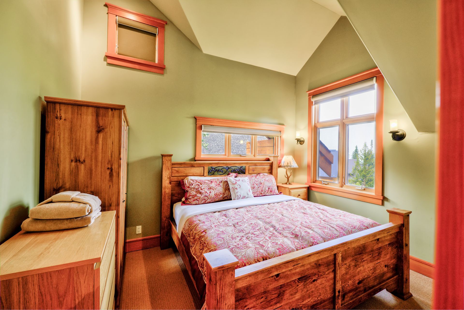Cozy wood-paneled bedroom with a queen bed, single bed, and two windows with red trim