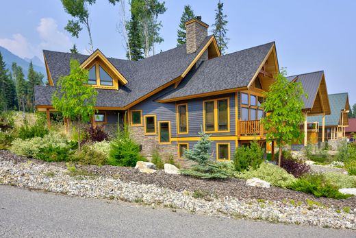 Modern rustic house with dark gray roof, yellow trim, stone landscaping, and trees in front