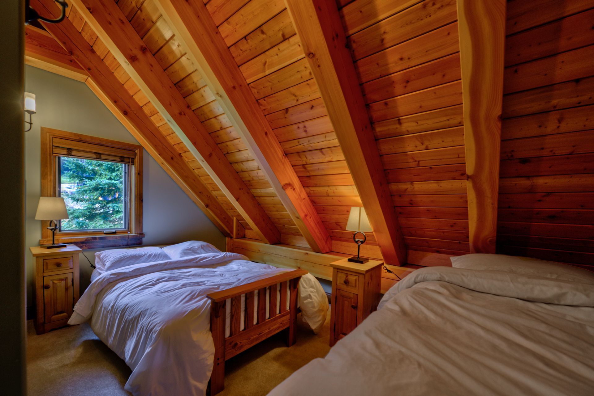 Cozy wooden attic bedroom with two twin beds and a window overlooking greenery
