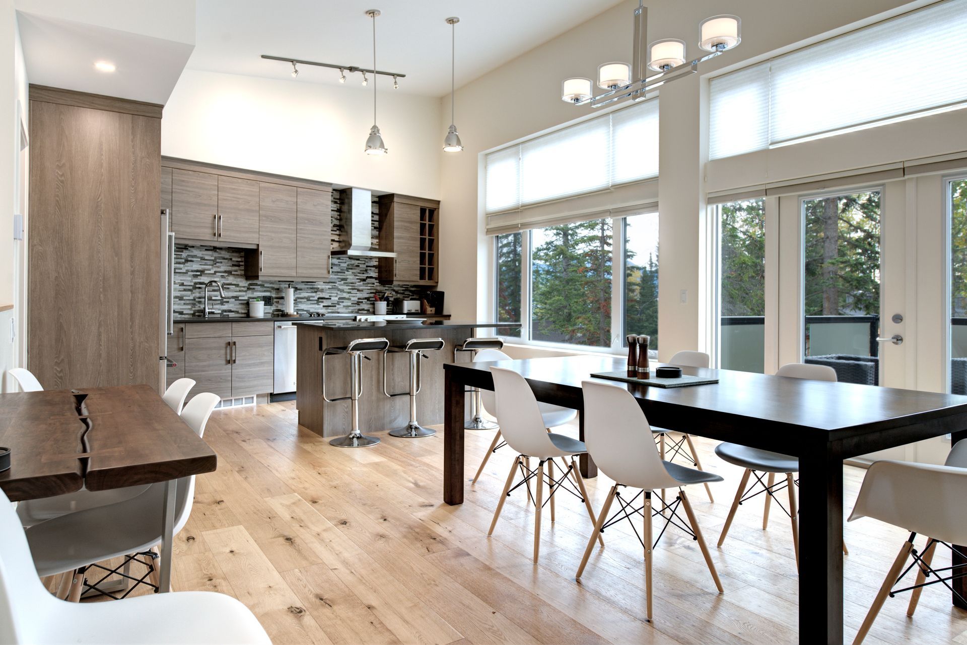 Modern open-concept kitchen and dining area with large windows, black table, white chairs, and wood floors