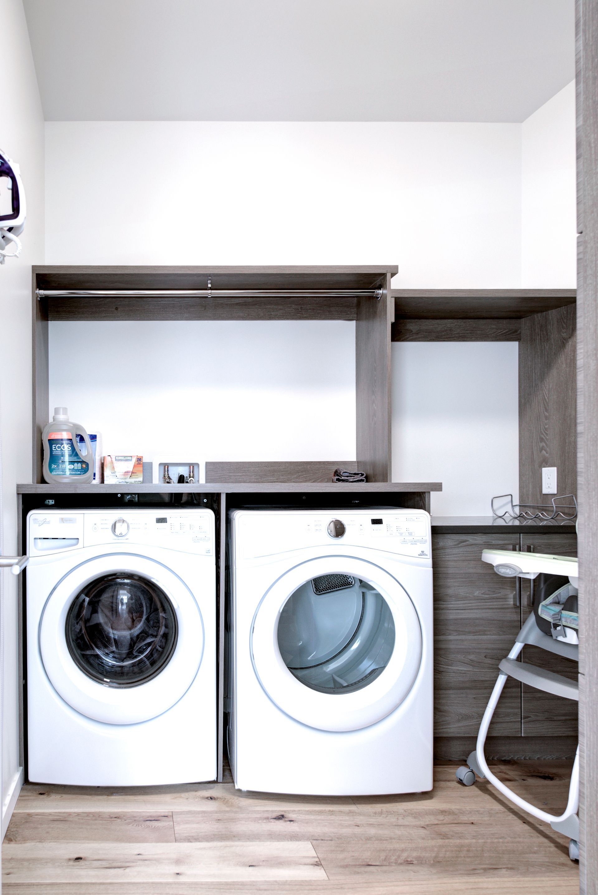 Laundry area with two front-loading washers under a counter and open shelving above.