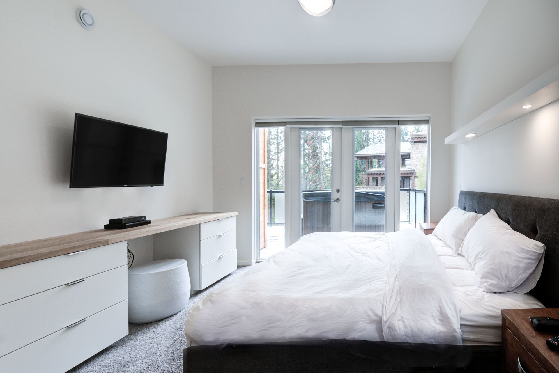 Modern bedroom with a bed, wall-mounted TV, dresser, and sliding glass doors to a patio.