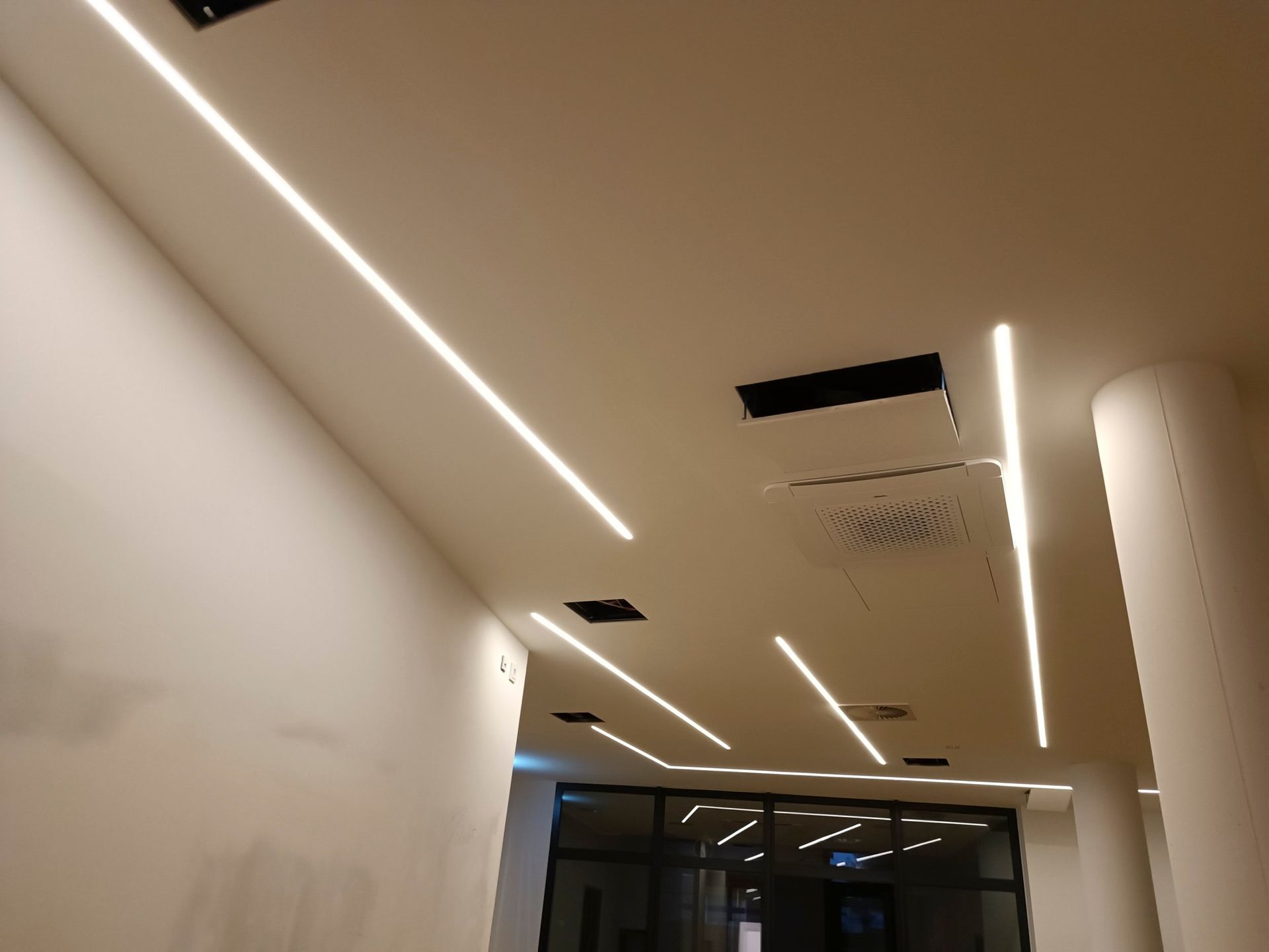 Weiße Decke mit linearen LED-Leuchten in einem Flur.