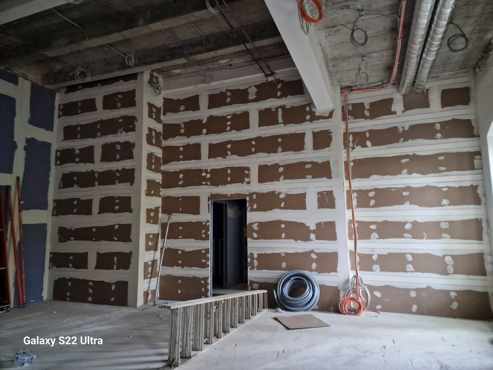 Innenraum im Bau, mit freiliegender Trockenbauwand und elektrischen Leitungen an den Wänden.