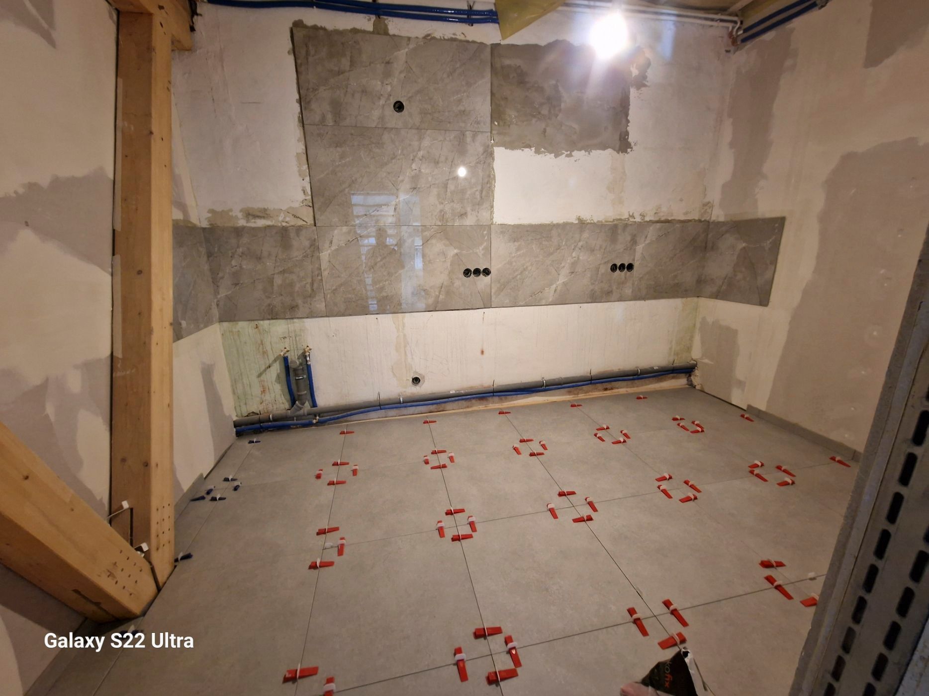 Im Bau befindliches Zimmer mit Fliesenboden. Graue und weiße Wände, freiliegende Holzbalken.