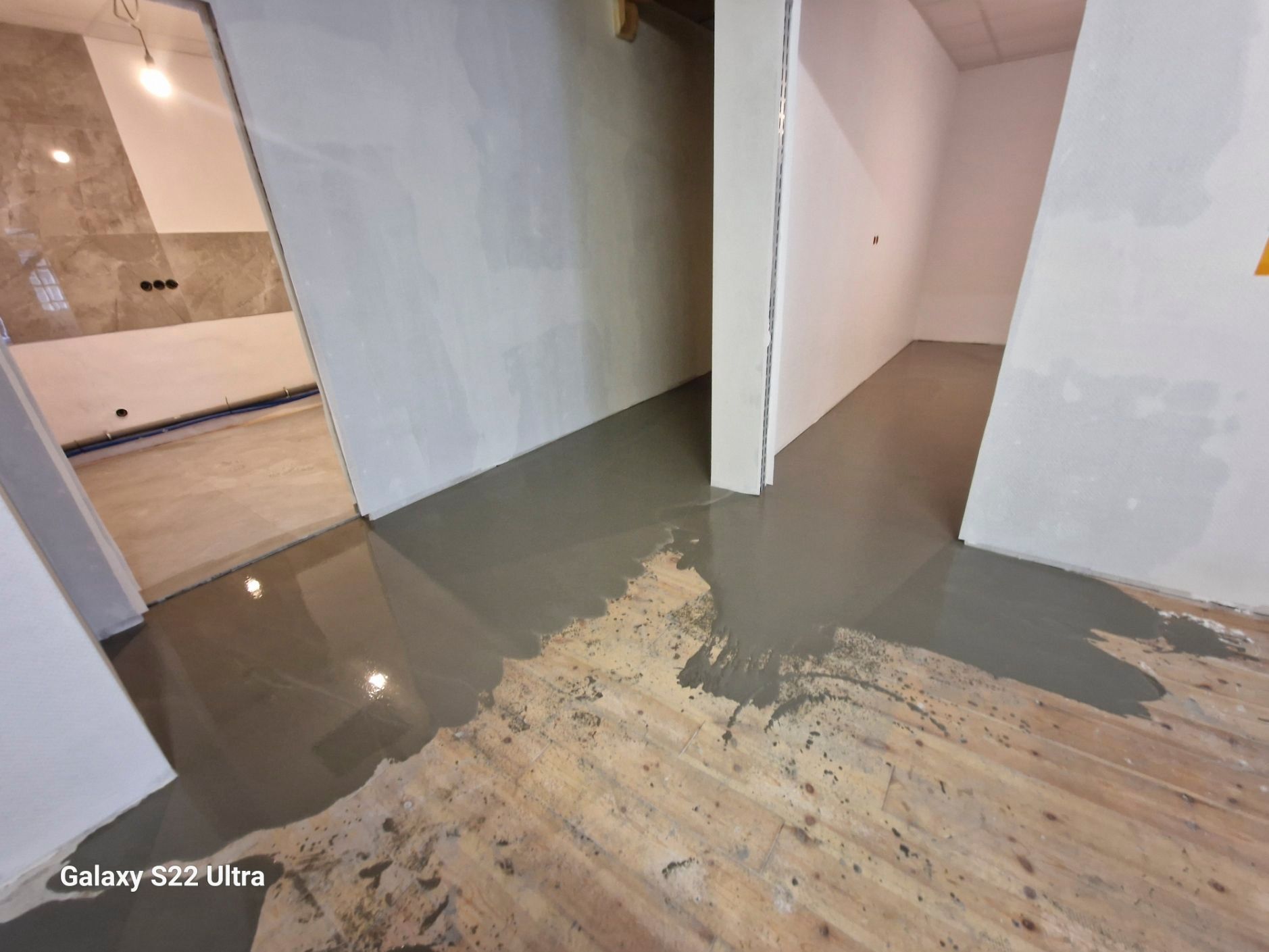 Eine graue flüssige Bodenbeschichtung, die in einem im Bau befindlichen Raum mit einer Türöffnung aufgetragen wurde.