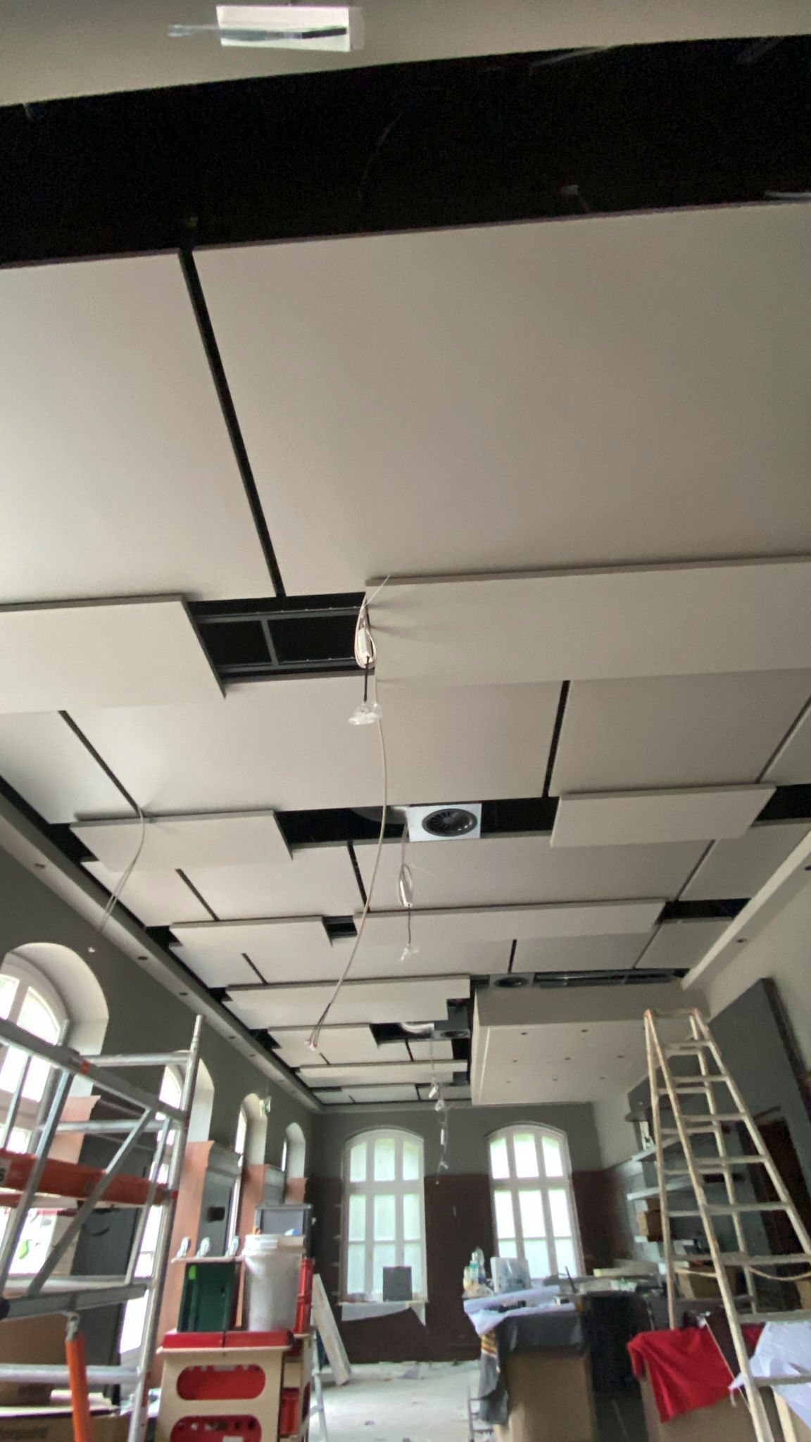 Konstruktion auf einer abgehängten Decke mit quadratischen weißen Paneelen und schwarzen Stützbalken.