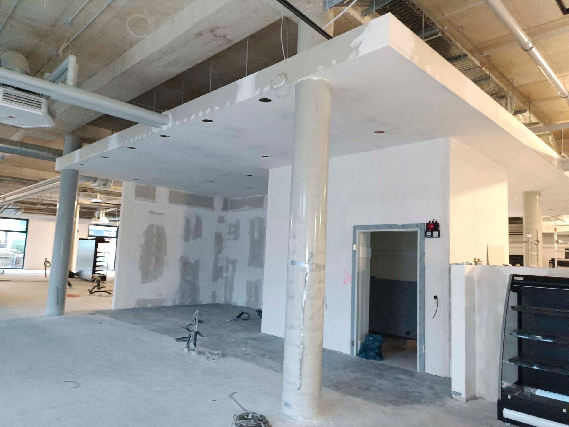 Innenbaustelle. Weiße Wände und Säulen, freiliegende Decke, Betonboden, Türöffnung.