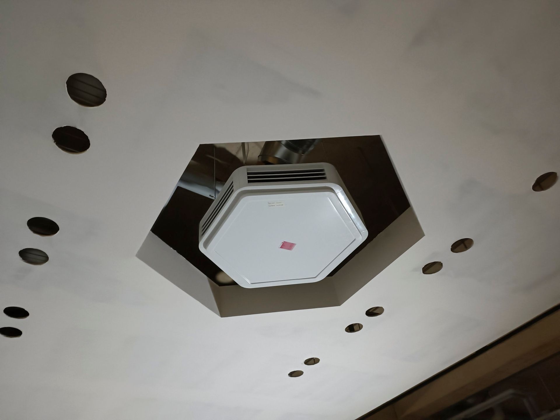 Weiße Decke mit einem sechseckigen Loch, in dem sich eine weiße, sechseckige Leuchte befindet. Mehrere kleinere runde Löcher umgeben die Leuchte.