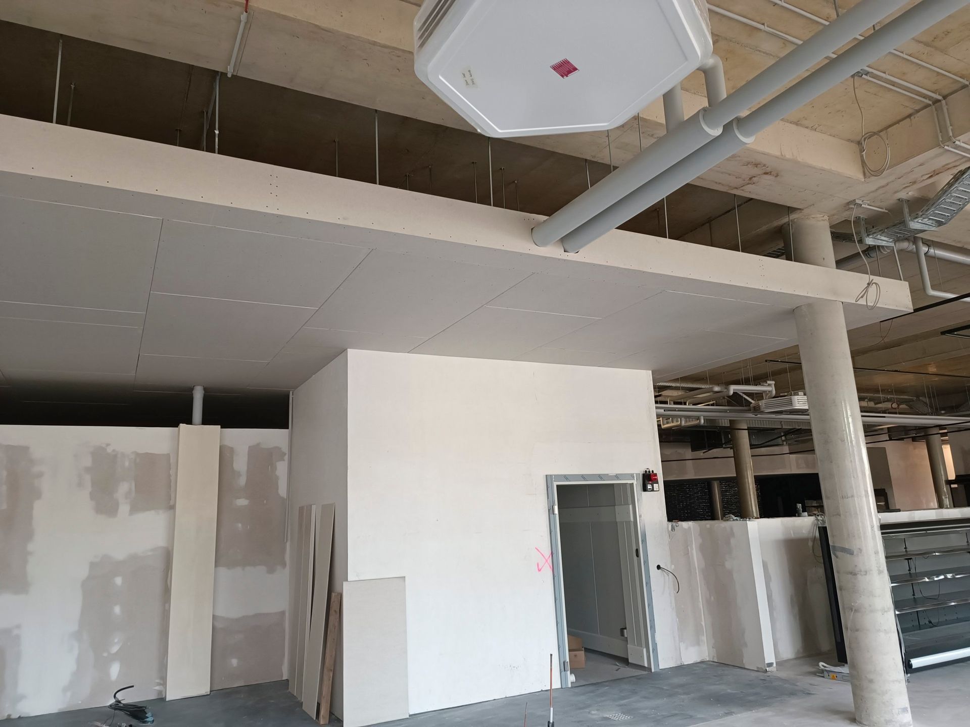 Innenansicht einer Baustelle mit Wänden und Decken aus Trockenbau, freiliegenden Rohren und einem Türrahmen.