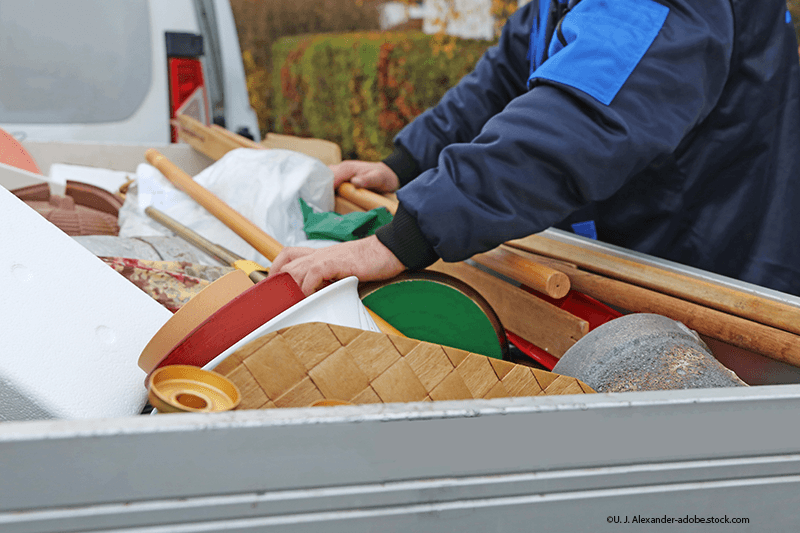 Eine Person in einer blauen Jacke sortiert Haushaltsgegenstände und Werkzeuge, die auf der Ladefläche eines Lastwagens verladen sind.