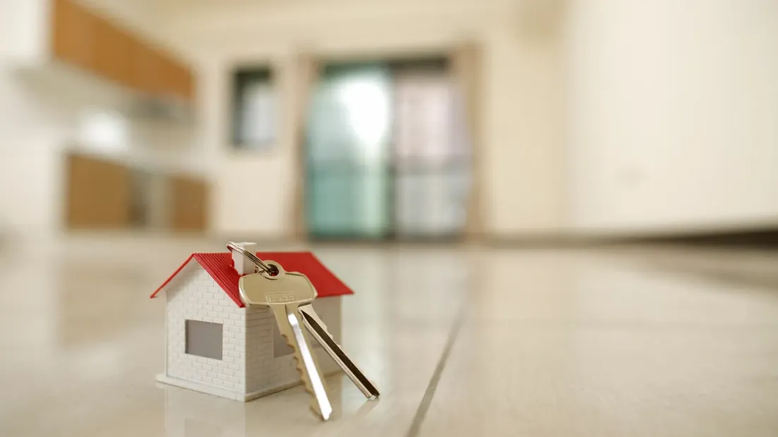 Casa en miniatura con llaves sobre un suelo brillante, interior borroso en el fondo.