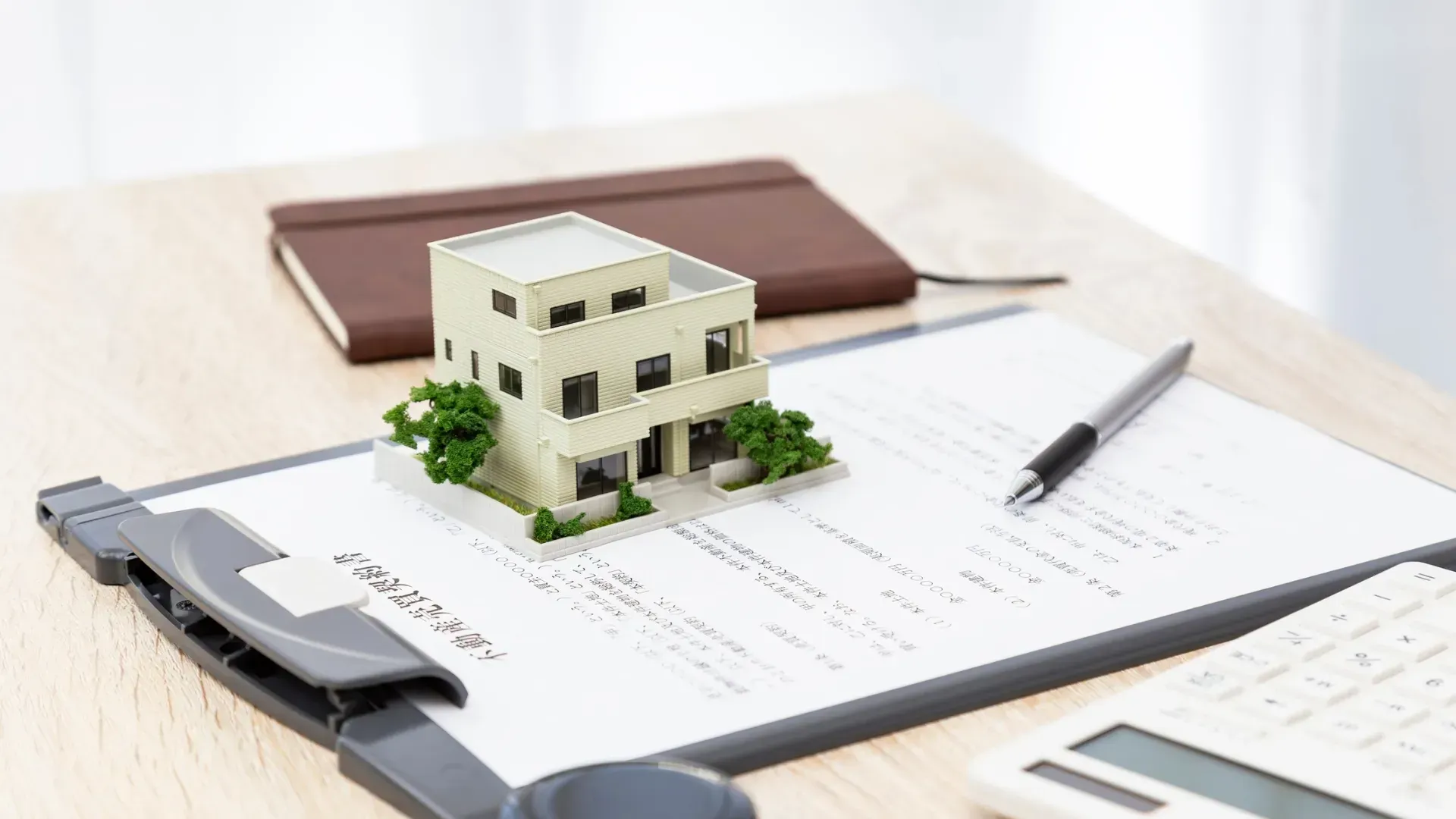 Una casa modelo se encuentra sobre un documento inmobiliario con un bolígrafo y un bloc de notas.