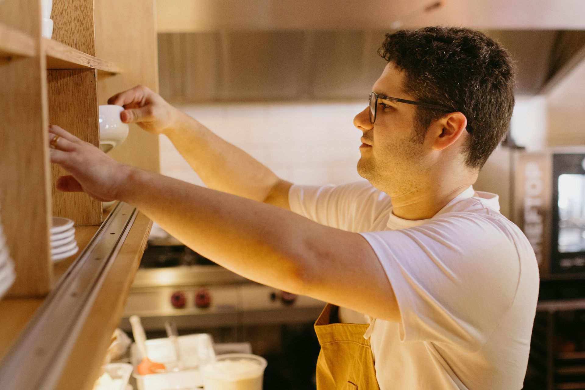 Um homem está pegando algo em uma prateleira na cozinha.