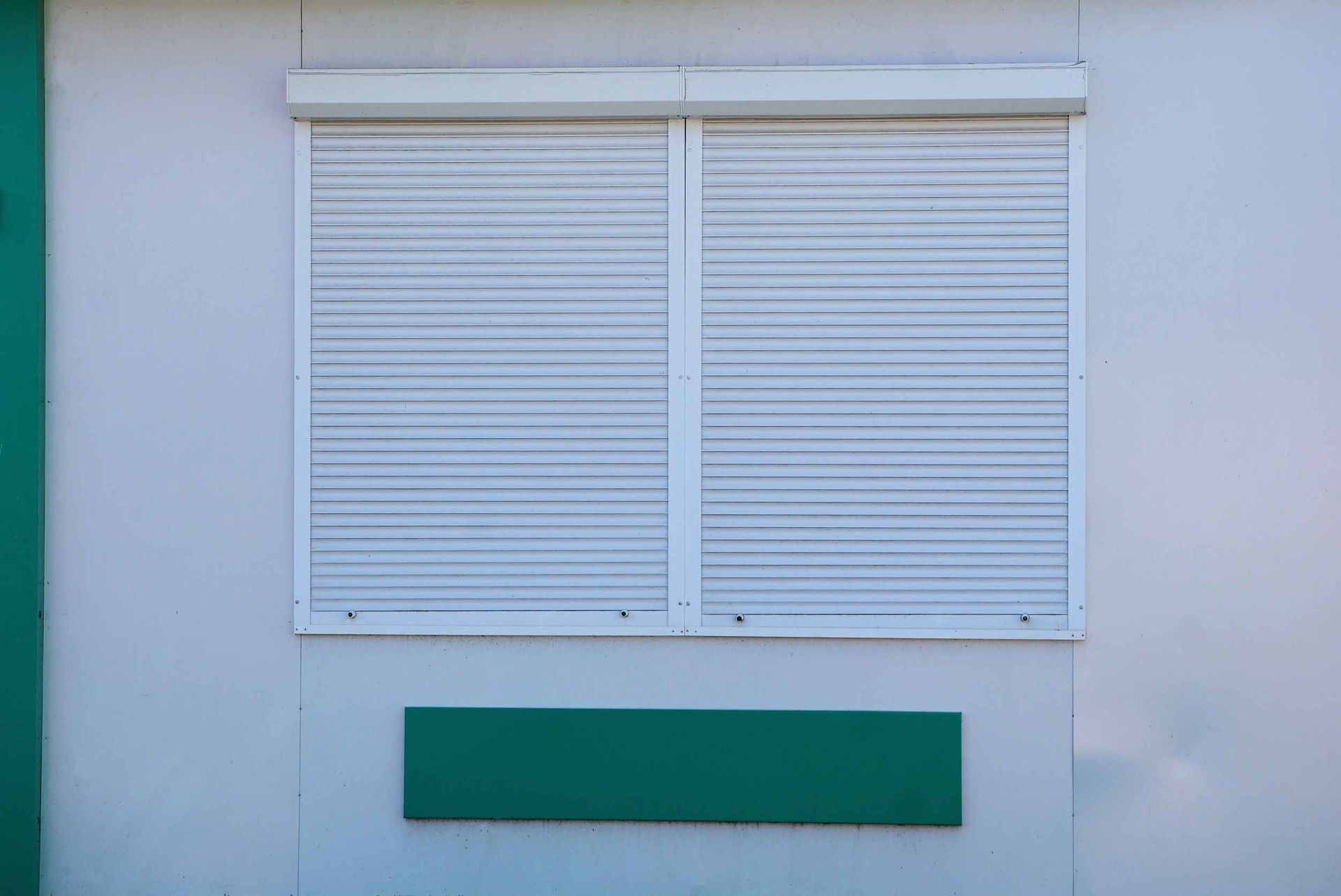 Un edificio blanco con detalles verdes y una ventana blanca con persianas enrollables.