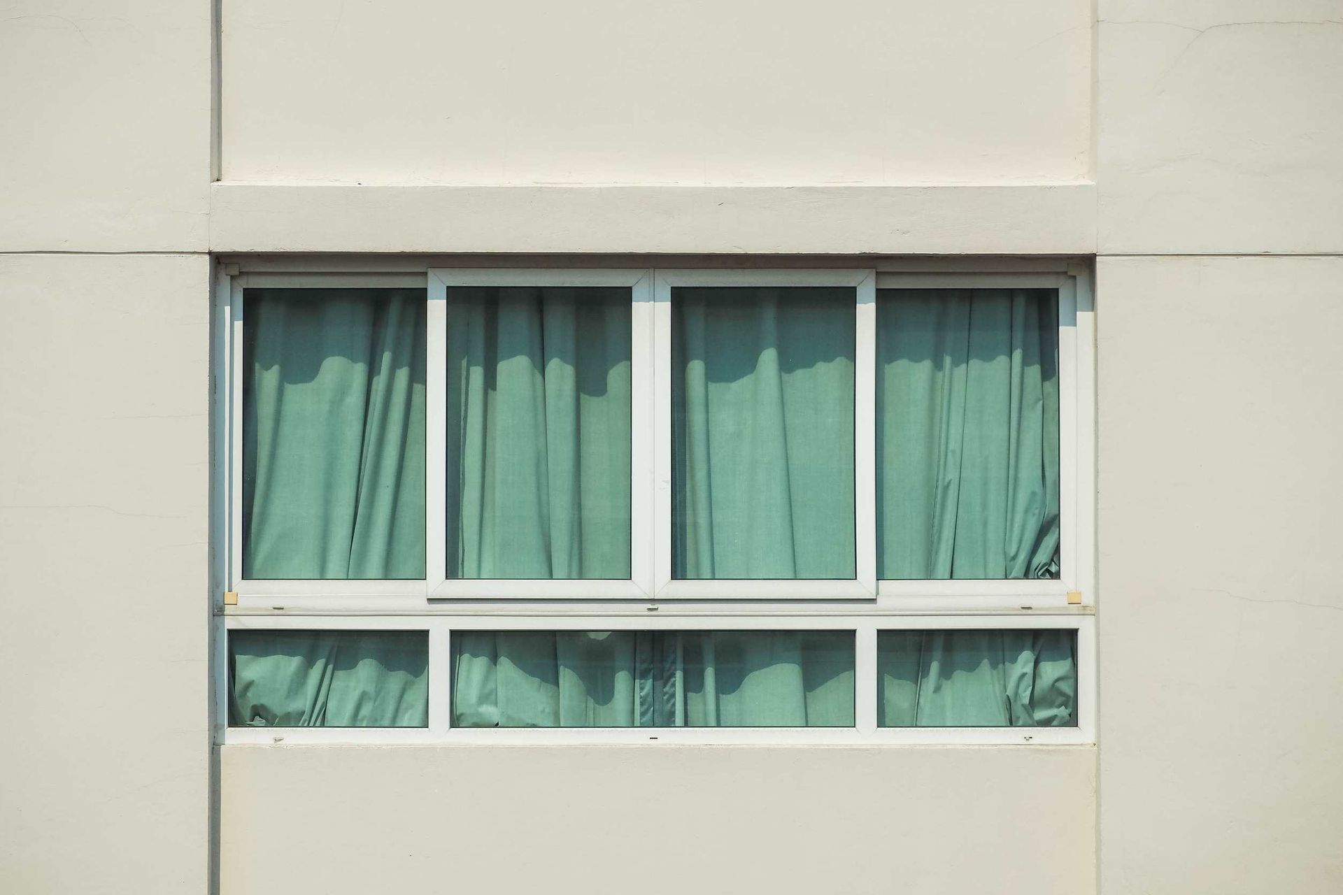 Una ventana blanca con cortinas verdes en una pared blanca.