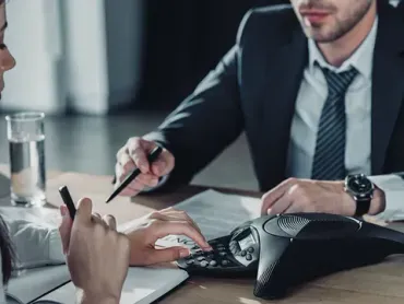 Un hombre con traje y corbata está sentado en una mesa con una mujer que usa una calculadora.