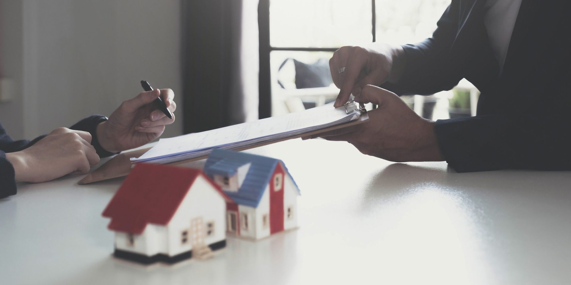 Un hombre y una mujer están sentados en una mesa con casas en miniatura y un portapapeles.