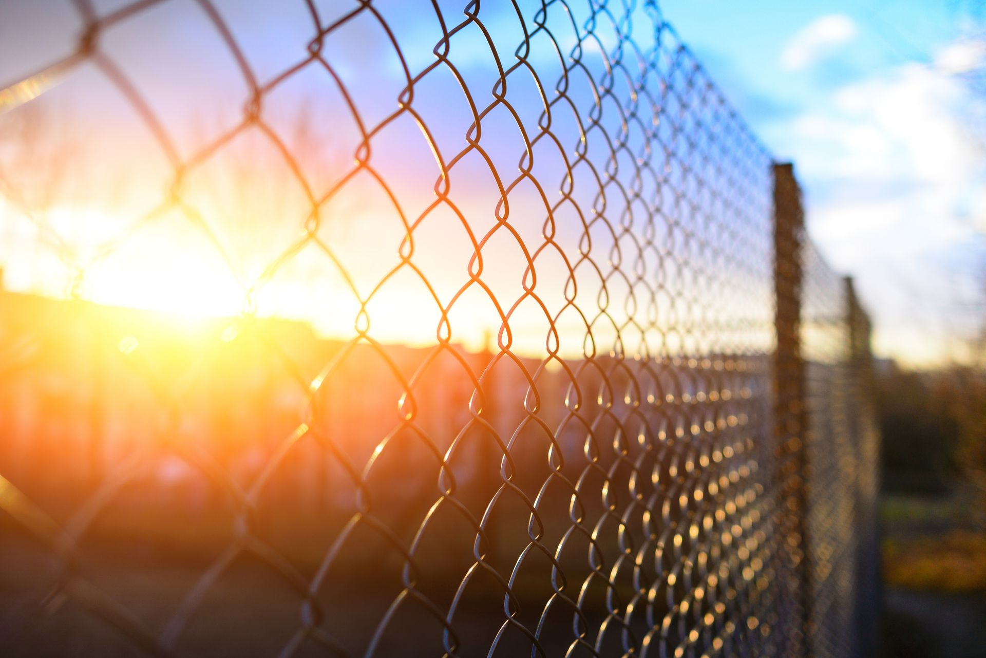 Le soleil brille à travers une clôture grillagée, à l'extérieur, ciel bleu, lumière dorée.